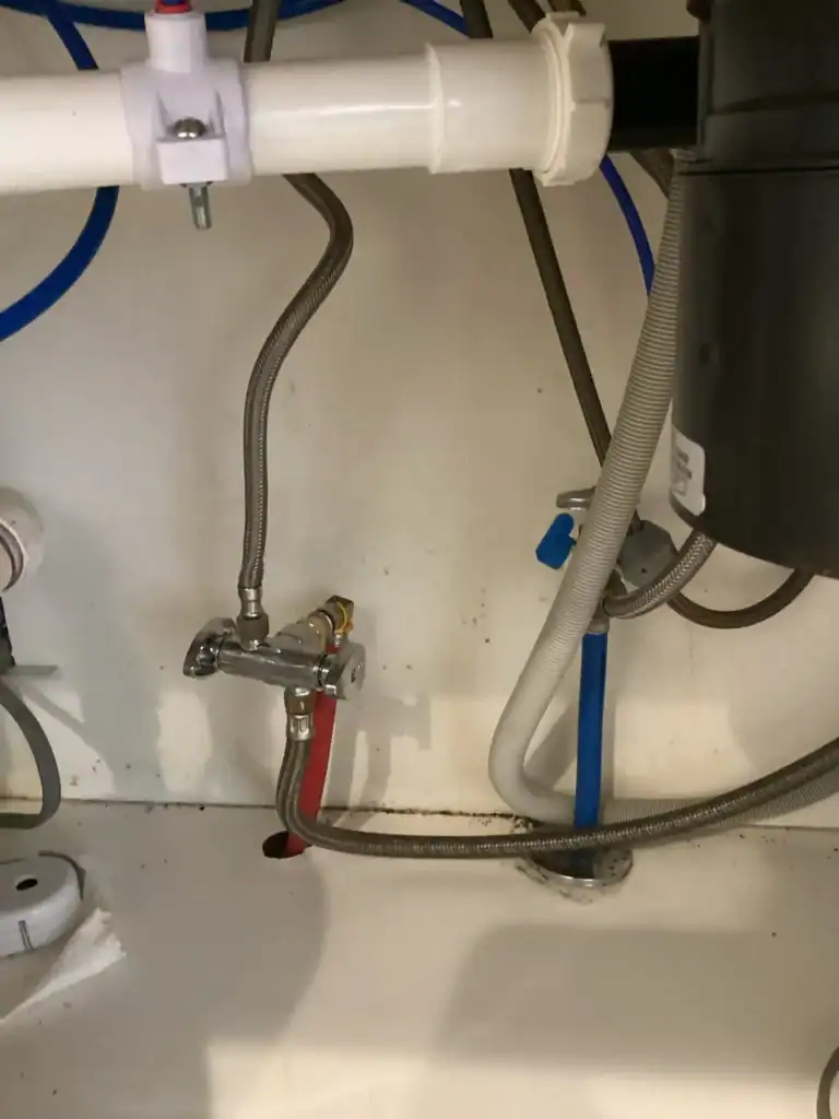 A clear view of under-sink plumbing featuring Holloway Plumbing’s expert installation, including water pipes, flexible hoses, accessible shutoff valves, and a garbage disposal unit. The setup displays an easy-to-identify red pipe for hot water and a blue pipe for cold water. Regular inspection of this area is recommended by Holloway Plumbing as part of your fall plumbing checklist to keep homes in Kerrville, TX running smoothly.